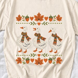 Three white ducks in striped scarves with acorn and maple leaf borders, retro screen print fall t-shirt art