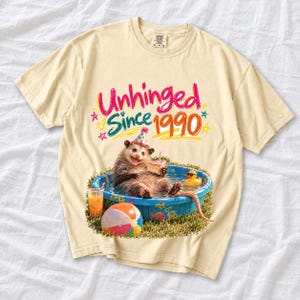 Opossum in party hat in a kiddie pool with cake, 90s film photo style, text "Unhinged Since 1990"
