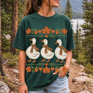 Three white ducks in striped scarves with acorn and maple leaf borders, retro screen print fall t-shirt art