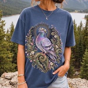 Painted pigeon wearing a daisy crown and glowing halo standing on a fern frond, whimsical cottagecore bird t-shirt art