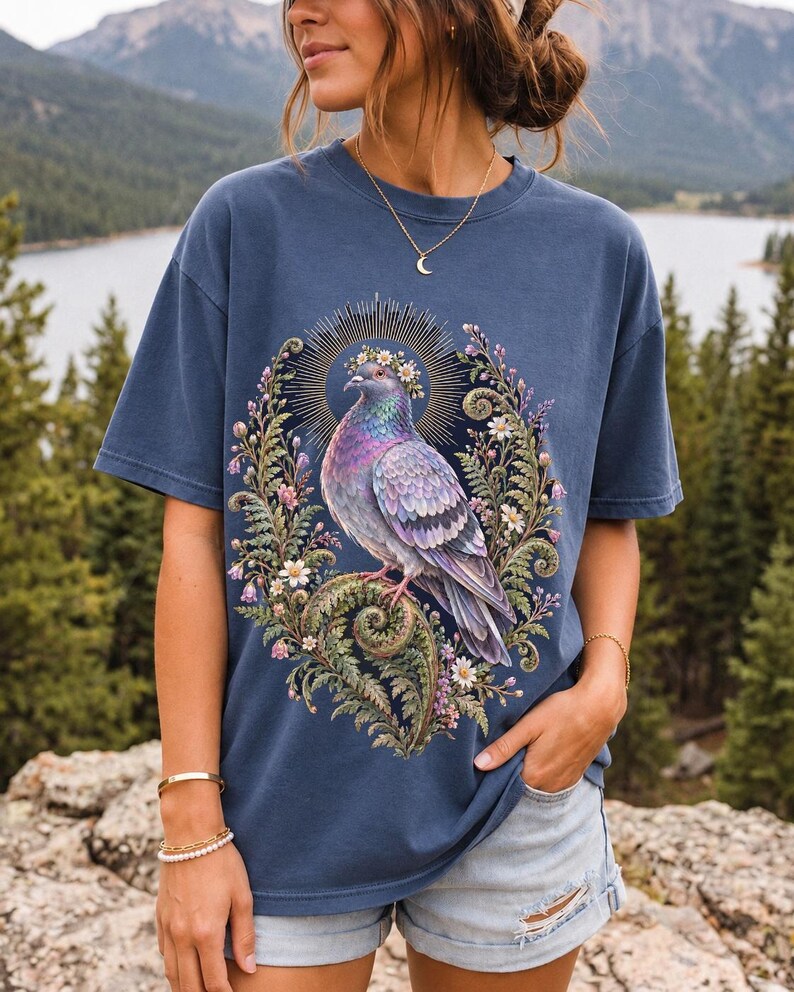Painted pigeon wearing a daisy crown and glowing halo standing on a fern frond, whimsical cottagecore bird t-shirt art