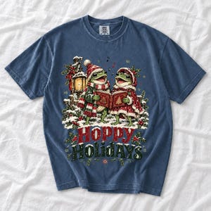 Two frogs singing carols in the snow with a lantern and songbook, text Hoppy Holidays