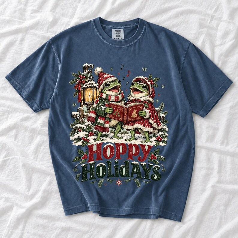 Two frogs singing carols in the snow with a lantern and songbook, text Hoppy Holidays