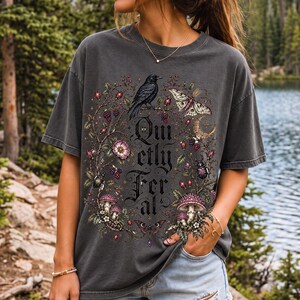 Raven on a wild rose branch with beetles and berries around blackletter text "Quietly Feral"