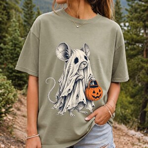 Etched pen illustration of a small mouse in a sheet ghost costume holding a candy bucket, bone white with orange accent
