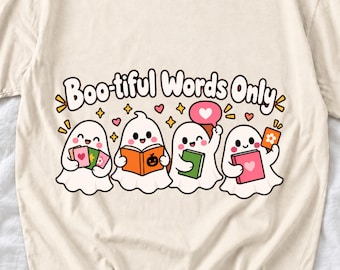 May include: A cream-colored t-shirt featuring a graphic of four white ghosts reading books. The text above the ghosts reads "Boo-tiful Words Only" in black letters. The design includes small pink hearts, orange stars, and colorful books.