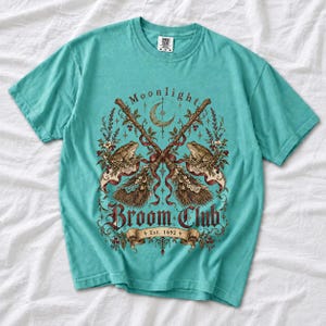 Vintage poster style crossed broomsticks with ribbons, lace and toads, text Moonlight Broom Club Est. 1692