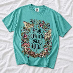 Victorian-style wreath of nightshade, luna moths and toadstools around the words "Stay Weird, Stay Wild"