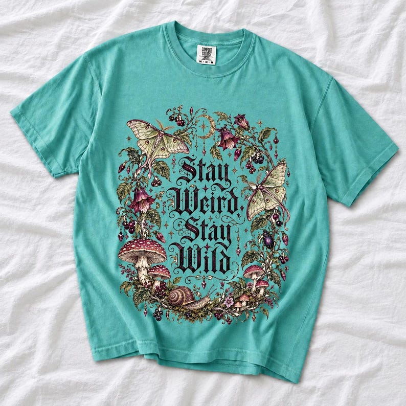 Victorian-style wreath of nightshade, luna moths and toadstools around the words "Stay Weird, Stay Wild"