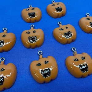May include: A collection of ten orange pumpkin charms, each featuring a glossy finish and a black painted jack-o'-lantern face with a wide, toothy grin. Each individual pumpkin charm includes a small silver-toned metal loop at the top for attachment.
