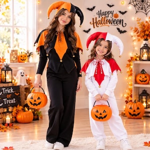 May include: Two individuals wearing jester-style Halloween costumes. One wears a black and orange outfit with a matching jester hat, while the other wears a white and red outfit with a matching jester hat. Both hold orange plastic pumpkin buckets.