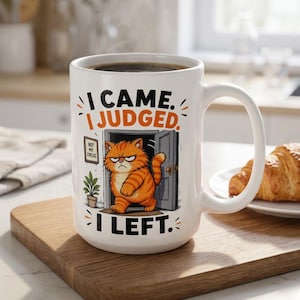 Peut inclure: Un mug en céramique blanche illustré d'un chat tigré orange sortant d'une porte avec une expression boudeuse. Le texte indique I CAME. I JUDGED. I LEFT. et un petit panneau mural affiche NOT MY CIRCUS. Le mug possède une anse sur le côté droit.