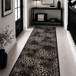 May include: A rectangular runner rug featuring a brown and black leopard print pattern with a solid black border. The rug is positioned lengthwise on a light-coloured floor, showcasing a repeating animal-inspired spotted design throughout.