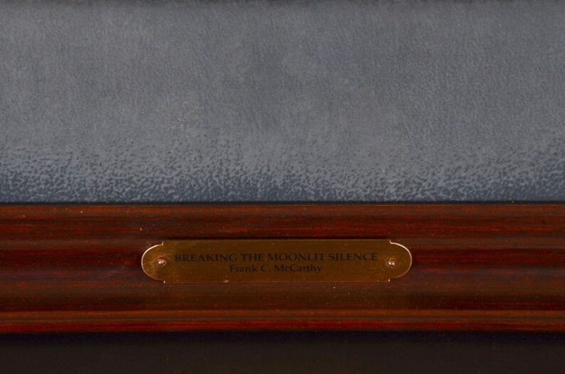 May include: A close-up of a wooden frame with a gold plaque that reads "Breaking the Moonlit Silence Frank C. McCarthy".