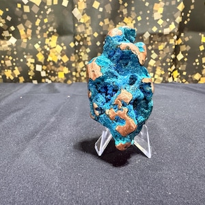 May include: A raw mineral specimen featuring a porous, textured structure with deep blue and vibrant turquoise crystalline formations interspersed with smooth, metallic copper-colored patches, displayed upright on a clear acrylic stand.