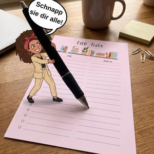 May include: A light pink TBR liste paper sheet featuring a cartoon character holding a large black pen with a speech bubble that says Schnapp sie dir alle. The sheet includes a row of colorful books and columns for Titel and Autor.in.