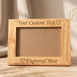 May include: A rectangular light brown wooden picture frame with a horizontal orientation. The top border is engraved with the text Your Custom Text and a heart symbol, while the bottom border features a heart symbol and the text Engraved Here.