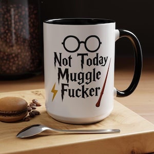 May include: A white ceramic mug with a black interior and handle. The front features black text that reads Not Today Muggle Fucker, accompanied by a graphic of round glasses, a yellow lightning bolt, and a brown wand with a dark tip.