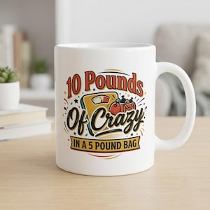 May include: A white ceramic mug featuring a graphic illustration of a yellow bathroom scale and a red gym bag. The text reads 10 Pounds Of Crazy IN A 5 POUND BAG in black, red, and yellow lettering, surrounded by small colorful confetti accents.