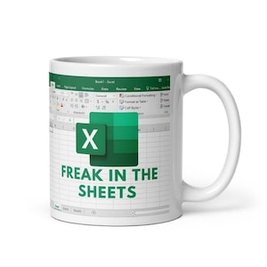 May include: A white ceramic mug featuring a printed graphic of a Microsoft Excel spreadsheet interface. The design includes the green Excel logo and the text "FREAK IN THE SHEETS" in bold green capital letters centered on the front of the mug.
