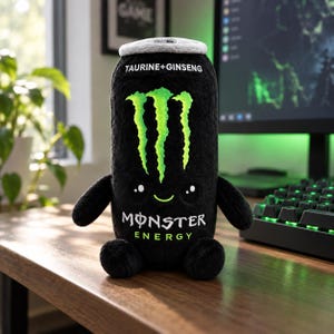 Peut inclure: Une peluche en forme de canette de boisson énergisante noire avec un dessus gris duveteux. Elle présente un logo griffe vert vif, le texte TAURINE+GINSENG et MONSTER ENERGY. La peluche a un visage brodé mignon avec deux yeux noirs et un petit sourire.