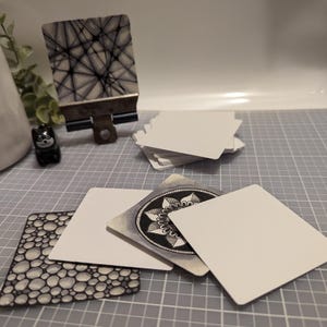 May include: A set of blank white cards with a black and white patterned card on a metal clip. The cards are on a gray grid surface.
