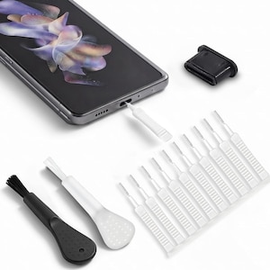 May include: A smartphone with a black screen, a black port plug, one black cleaning brush, one white cleaning brush, and ten small white interdental-style cleaning picks. One white pick is inserted into the smartphone charging port.