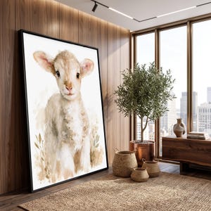 Könnte beinhalten: Ein großes gerahmtes Wandbild mit einer Aquarellillustration eines jungen Lamms mit weichem beigem und weißem Fell. Das Lamm ist in stehender Position vor einem hellen, neutralen Hintergrund mit zarten Blattmotiven am unteren Rand dargestellt.