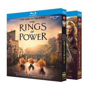 May include: Two Blu-ray disc cases for The Lord of the Rings: The Rings of Power. The front cover features a fantasy landscape with ships on water, the title text, and cast names. The side spines show a character portrait and series information.