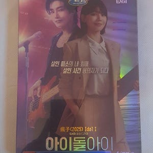 Peut inclure: Un boîtier de disque Blu-ray présentant une image promotionnelle de deux personnes. L'une joue de la guitare basse, tandis que l'autre porte un blazer beige. La couverture inclut le logo ENA, du texte coréen et le titre Idol I, avec un fini holographique.
