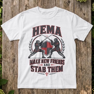 Könnte beinhalten: Ein weißes Kurzarm-T-Shirt mit einer Grafik von zwei Fechtern in dunkler Rüstung, die ihre Schwerter vor einem rot-schwarzen Schild kreuzen. Der Text HEMA steht darüber, und der Text MAKE NEW FRIENDS AND STAB THEM ist unter der Grafik abgedruckt.