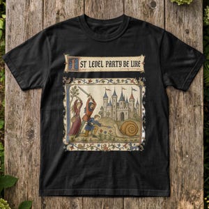 Puede incluir: Una camiseta negra con una ilustración de estilo medieval que muestra a tres figuras luchando contra un caracol gigante frente a un castillo. El texto "ST LEVEL PARTY BE LIKE" aparece en fuente gótica sobre la escena, que incluye bordes florales.
