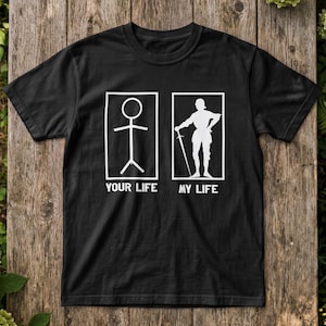 Może przedstawiać: Czarny t-shirt z krótkim rękawem z białym nadrukiem graficznym. Wzór przedstawia dwie prostokątne ramki z tekstem poniżej. Lewa ramka zawiera postać z kresek nad napisem YOUR LIFE, a prawa ramka przedstawia rycerza trzymającego miecz nad napisem MY LIFE.