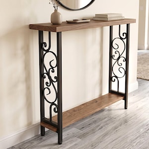 May include: A rectangular console table featuring a dark brown wooden top and a matching lower shelf. The frame is constructed from black metal with decorative scrollwork patterns on the sides, connecting the top and bottom surfaces.