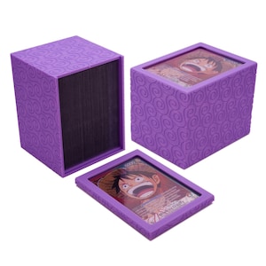 May include: A purple rectangular deck box with a textured spiral pattern on the exterior. The box features a removable lid with a clear window displaying a trading card of Monkey D. Luffy. The interior of the box is lined with black material.
