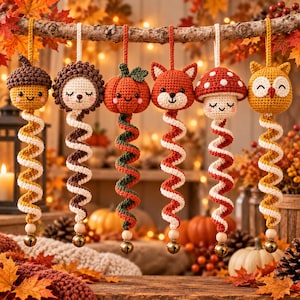 May include: Six crocheted hanging ornaments featuring an acorn, hedgehog, pumpkin, fox, mushroom, and owl. Each figure has a spiral tail in alternating colors, a hanging loop, and a small gold-toned metal bell attached to the bottom end.