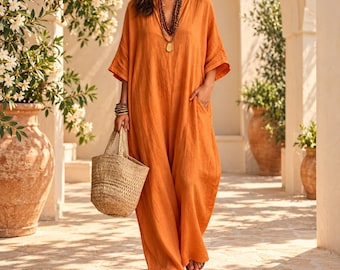 May include: A loose-fitting, floor-length orange dress with short sleeves and a V-neckline. The garment is paired with a multi-layered beaded necklace and a woven straw tote bag. The fabric has a textured appearance and a relaxed silhouette.