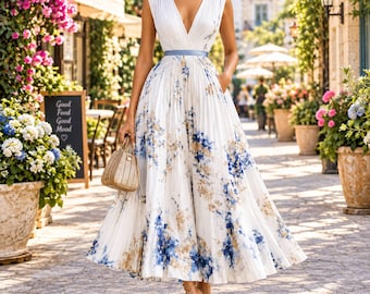 May include: A sleeveless white midi dress featuring a deep V-neckline, a pleated bodice and skirt, and a blue waist sash. The fabric is decorated with a blue and tan floral pattern. A small, textured, light-colored handbag is held at the side.