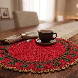 May include: A round, red crocheted placemat featuring a dark green leaf-like pattern around the perimeter and a gold-colored scalloped edge. A dark brown ceramic cup sits on a matching saucer, accompanied by a folded napkin and a small metal spoon.