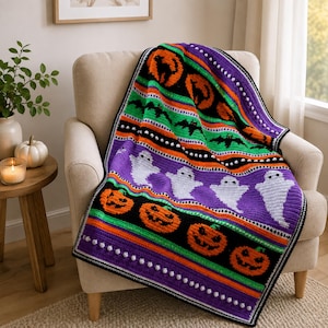 Könnte beinhalten: Eine gehäkelte Halloween-Decke mit horizontalen Streifen in Schwarz, Lila, Orange und Grün. Das Design zeigt wiederkehrende Muster aus orangefarbenen Kürbissen, weißen Geistern, schwarzen Fledermäusen und schwarzen Katzen mit weißen Noppenstichen.
