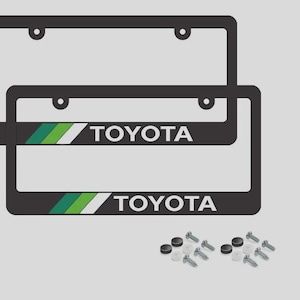 May include: Two black rectangular license plate frames featuring the white Toyota logo and a decorative stripe pattern in dark green, light green, and white. The set includes eight metal screws, eight black screw covers, and eight clear washers.