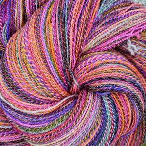 May include: A skein of hand-dyed yarn featuring a vibrant, variegated color palette of magenta, bright orange, deep purple, and teal. The twisted fiber displays a complex, multi-colored pattern with thin, tightly spun strands throughout the entire bundle.