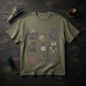 Peut inclure: Un t-shirt vert olive orné d'une grille de neuf illustrations comprenant un chaudron, un balai, un croissant de lune, un chat noir, une fiole étiquetée Witch's Brew, un hibou, un pentagramme, une plume et une toile d'araignée, avec des nœuds.