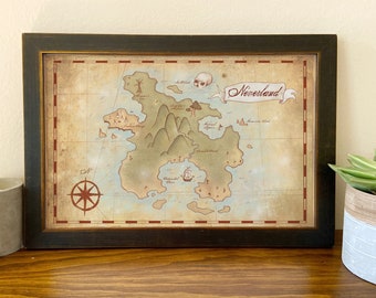 May include: A vintage-style map of Neverland, framed in a dark wood frame. The map features a detailed illustration of the island, including mountains, a lagoon, and a pirate ship. The title "Neverland" is written in a red banner at the top of the map.
