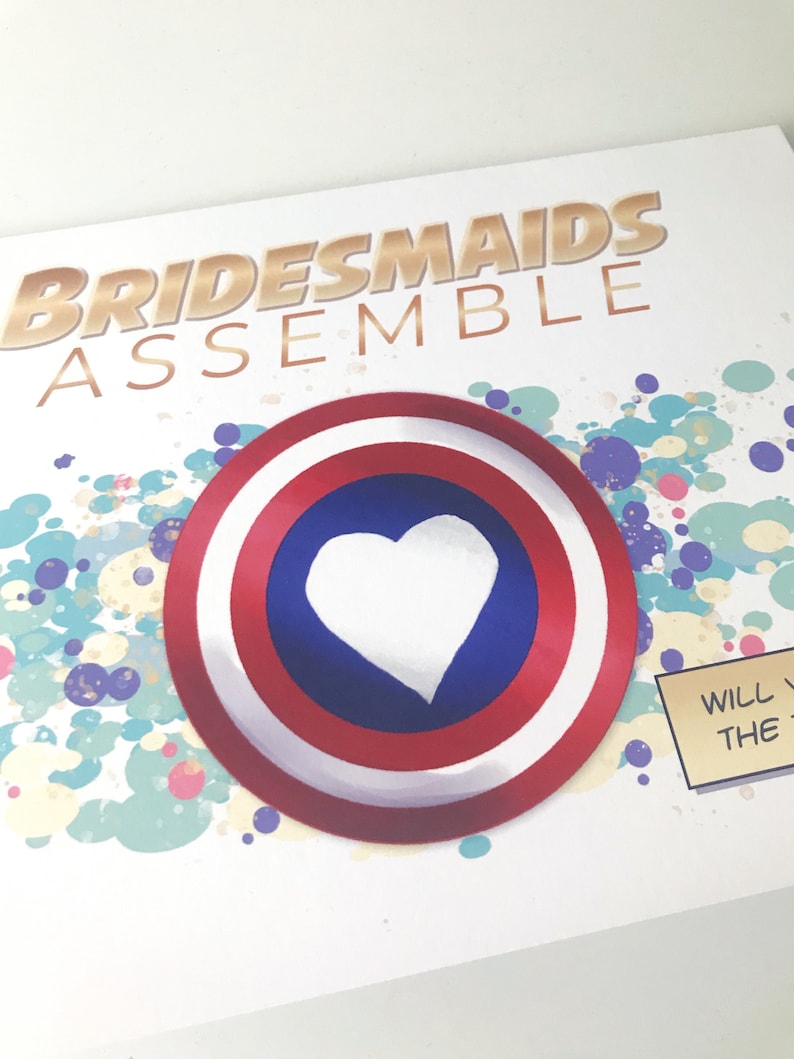 May include: A white card with the text "Bridesmaids Assemble" in gold letters. A red, white, and blue circle with a white heart in the center is on the card. The background is a colorful abstract design.