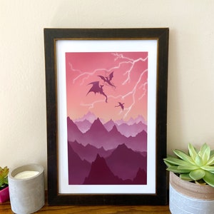 May include: A framed print of a digital illustration depicting three dragons flying through a pink and purple mountain range with lightning strikes in the sky.