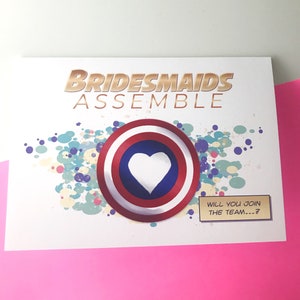 May include: A white card with the text "Bridesmaids Assemble" in gold lettering. A red, white, and blue circle with a white heart in the center is on the card. The text "Will you join the team...?" is in a comic book style speech bubble.