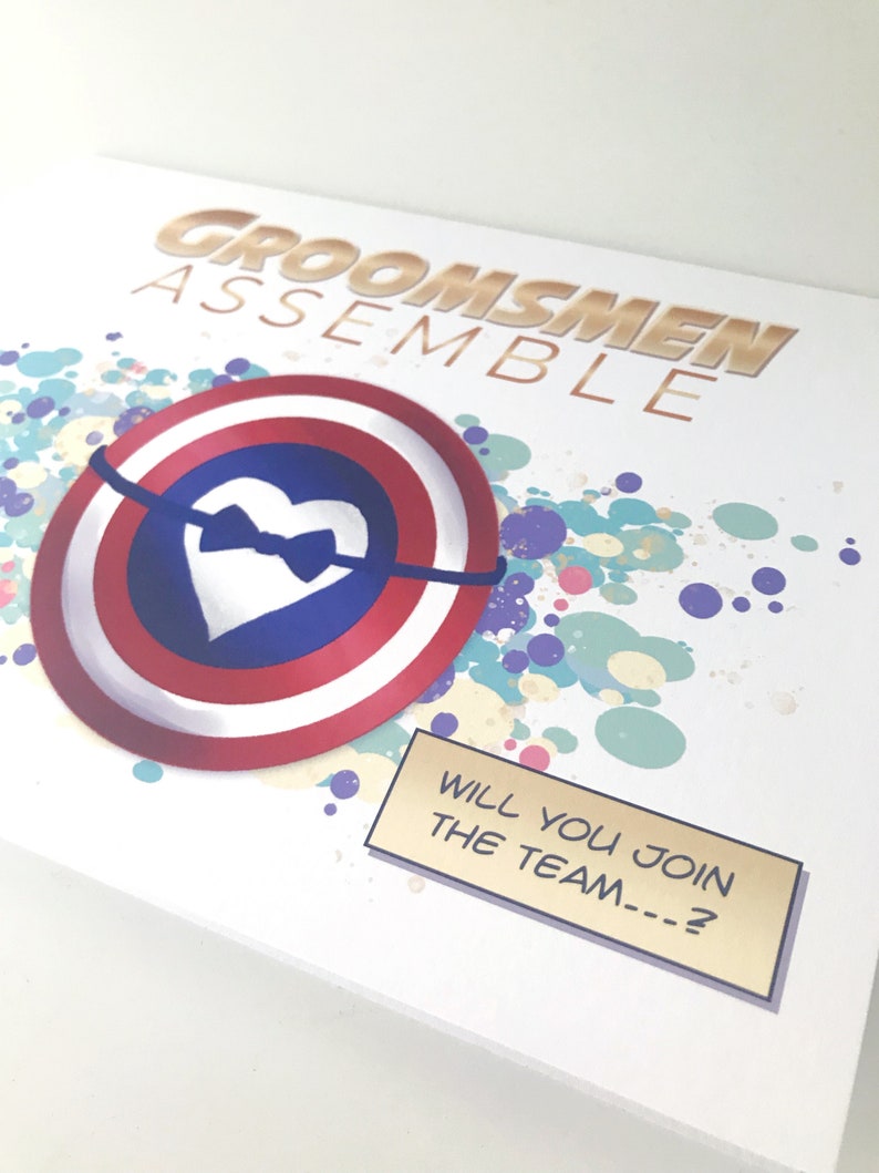 May include: A white card with a gold and red shield with a white heart and a black bow tie. The background is a colorful splatter pattern. The text "Groomsmen Assemble" is at the top of the card. The text "Will you join the team...?" is in a gold box with a black border.