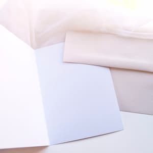 May include: A white card with a folded edge, and a blank white envelope on a white surface.