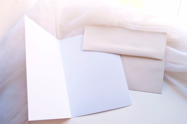 May include: A white card with a folded edge, and a blank white envelope on a white surface.